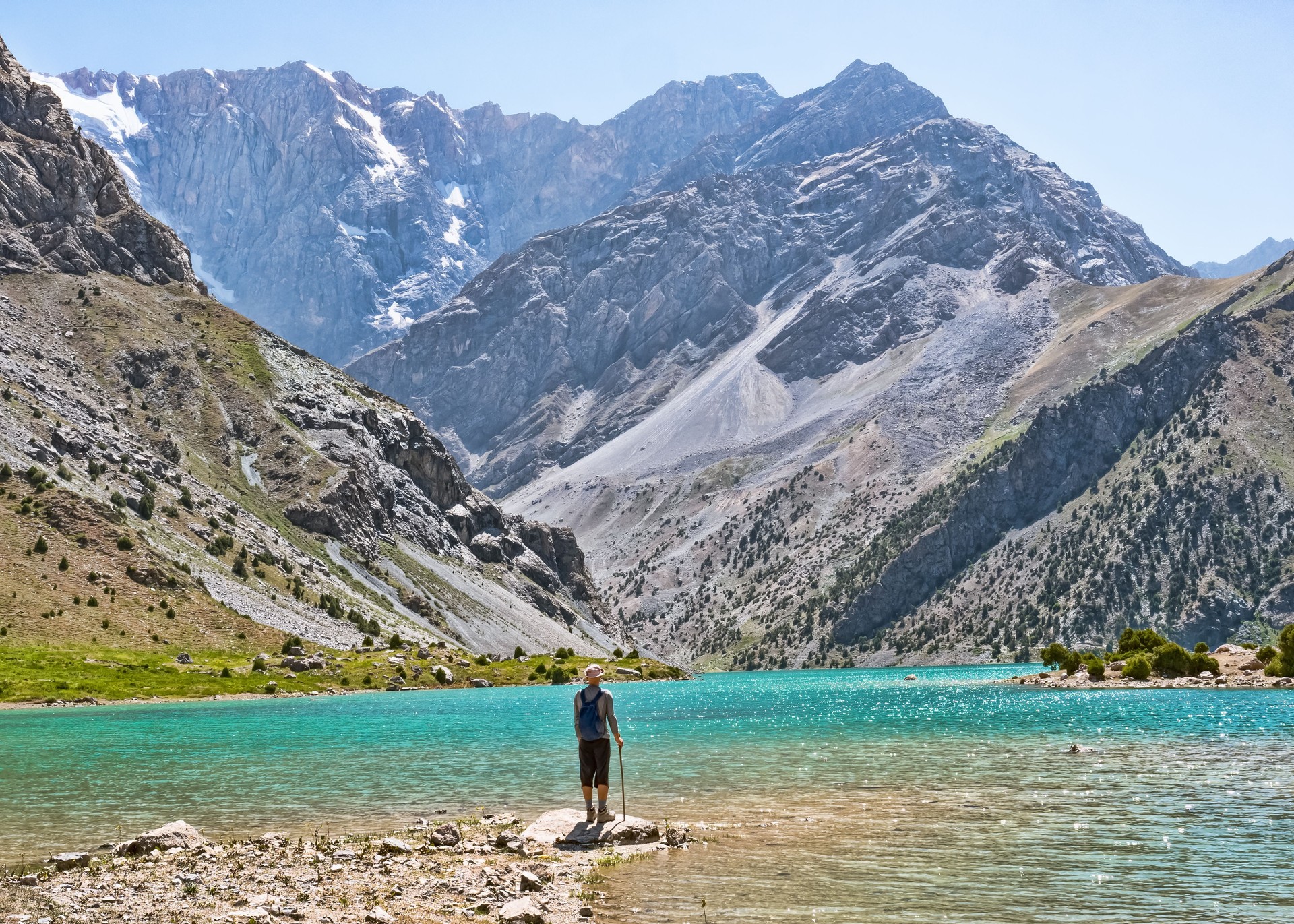 Hiker with backpack near Kulikalon lake on rocky mountain background. Fann Mountains, Tajikistan, Central Asia