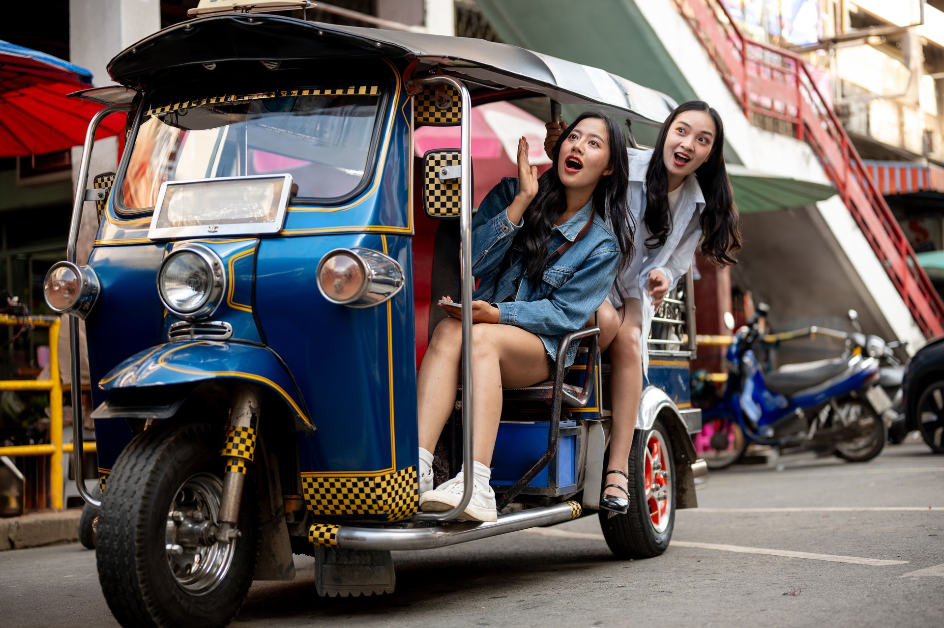 Two excited Asian girls enjoy a ride in a tuk-tuk in Thailand, amazed by the stunning views.