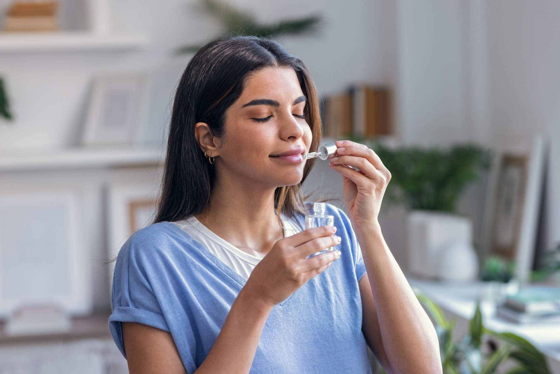 Beautiful woman holding a bottle of essential oil while testing it at home.